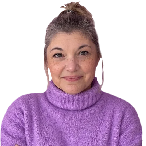 Woman with light skin and freckles wearing a purple turtleneck sweater, smiling and posing with arms crossed.